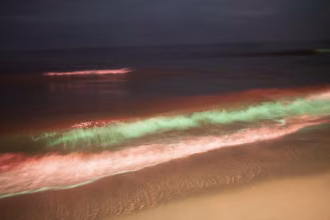Digitale Fotografie, verfremdester winterlicher Meeressaum, beleuchtete Wellen in grün und rot, Sandstrand, Horizont in schwarzblau, Usedom, Ostsee